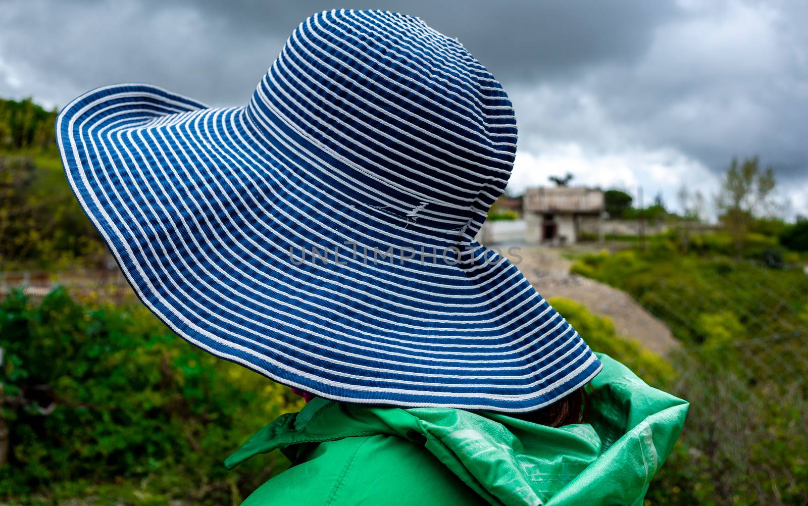 A girl in a wide-brimmed striped hat is watching the countryside