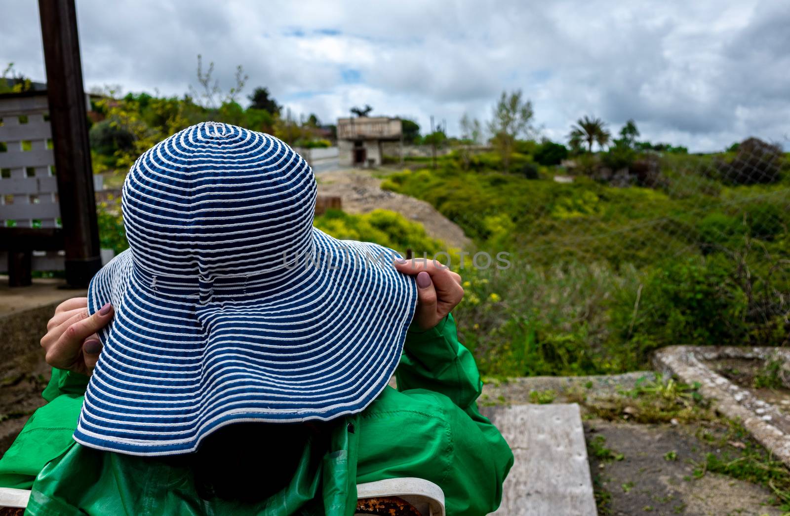 A girl in a wide-brimmed striped hat is watching the countryside