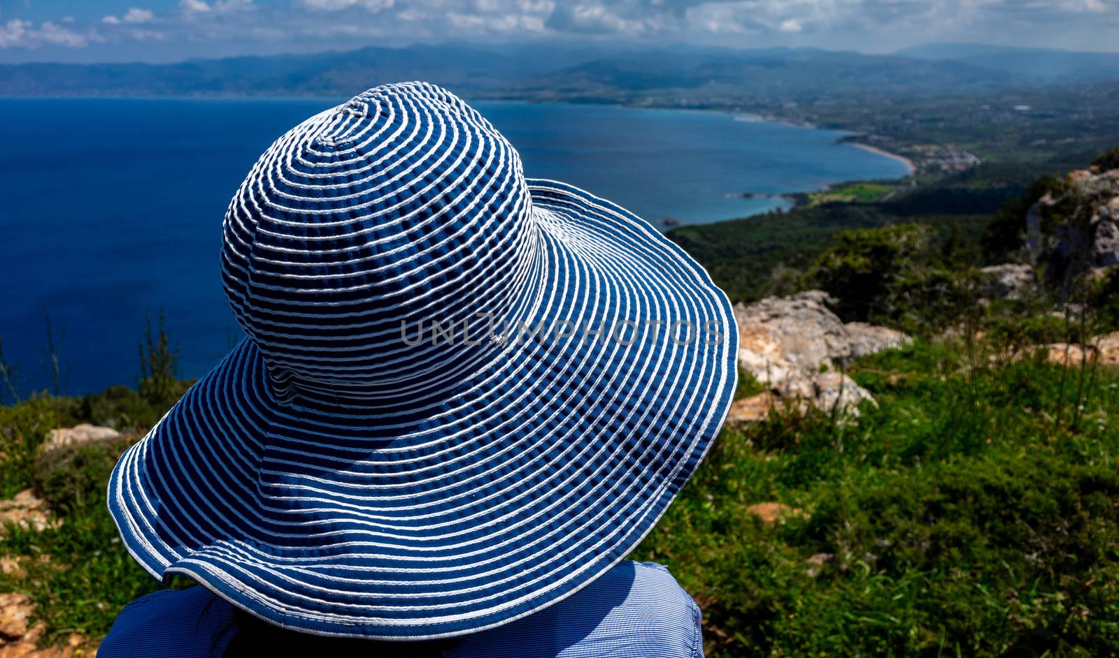 A girl in a wide-brimmed striped hat looks at the beautiful landscape of the coastline