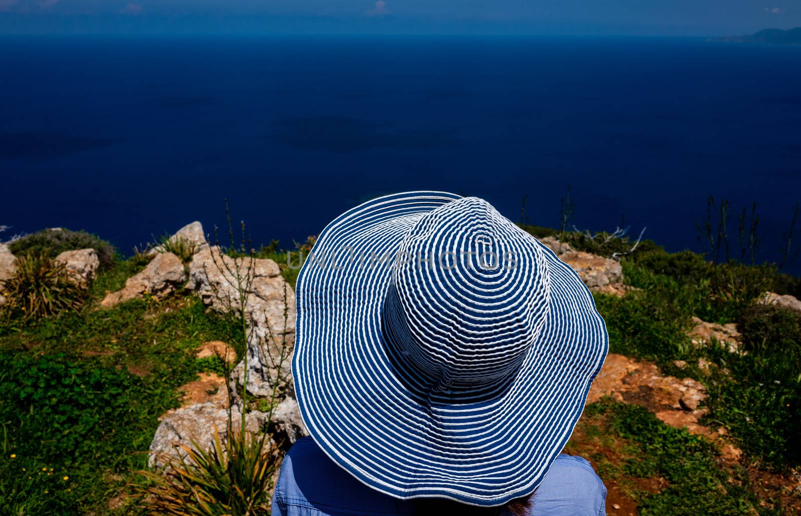 A girl in a wide-brimmed striped hat looks at the beautiful landscape of the coastline