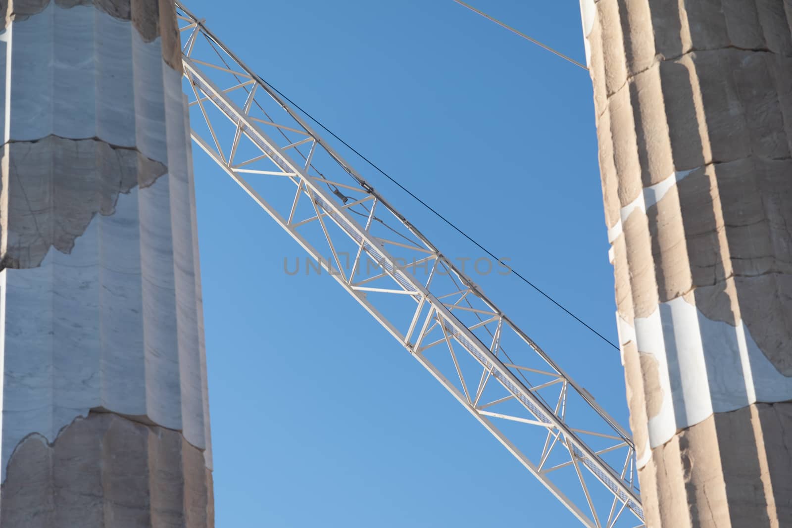 A construction crane behind old stone pillars with a bright blue sky in the background
