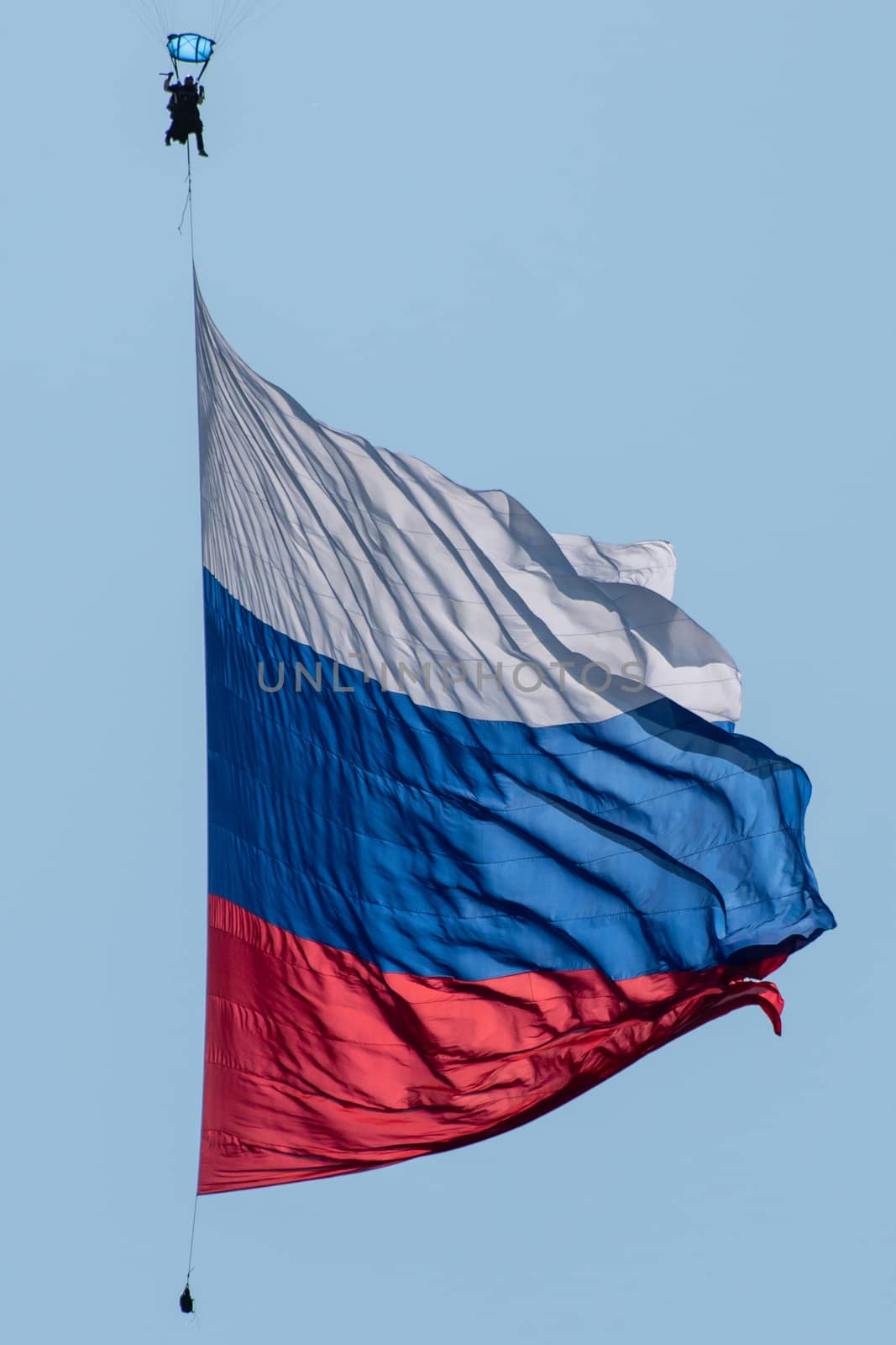 Skydiver in the sky with a giant flag of Russia against the blue sky.