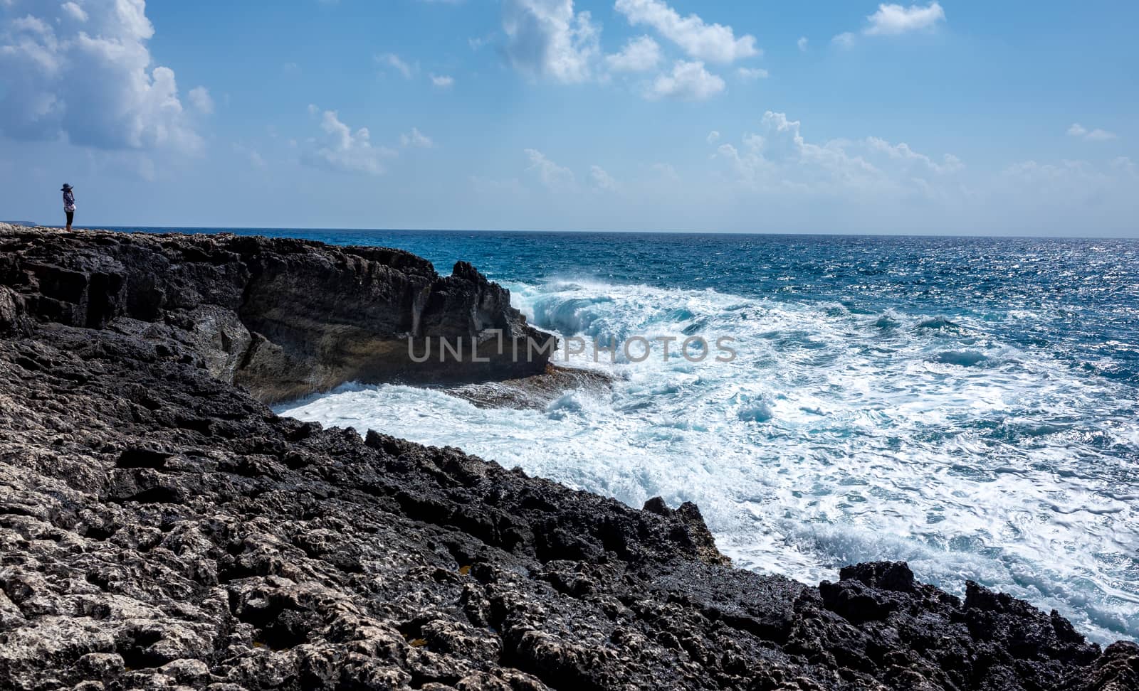 A girl on the beach watches the waves breaking on the rocky shore of the Mediterranean Sea on the Akamas Peninsula in the northwest of the island of Cyprus.