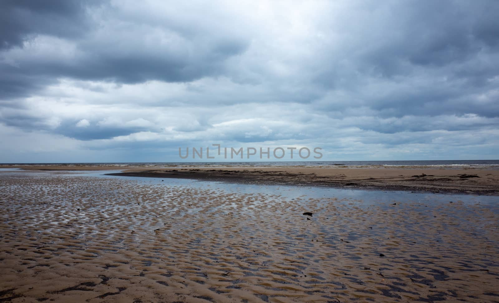 Reflection of clouds in a small lehman on the sandy shore of the Baltic Sea in Jurmala in cloudy weather.