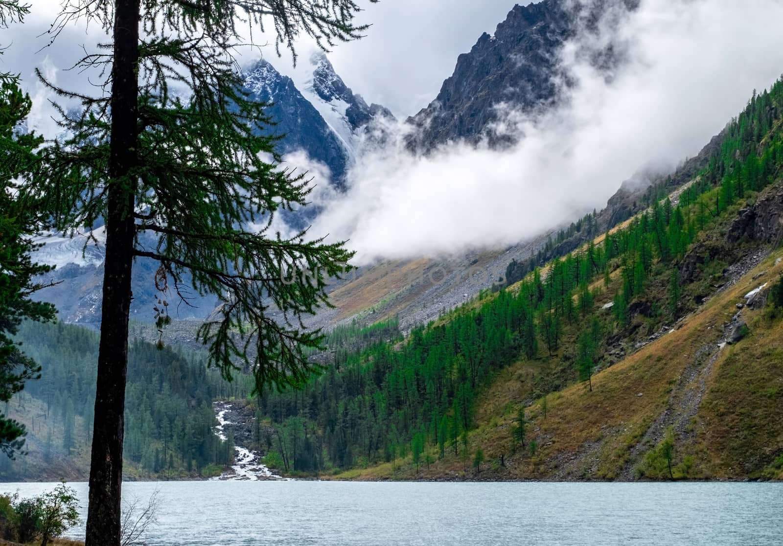 Shavlinskoye lake in the Altai Republic on the background of mountain peaks shrouded in fog.