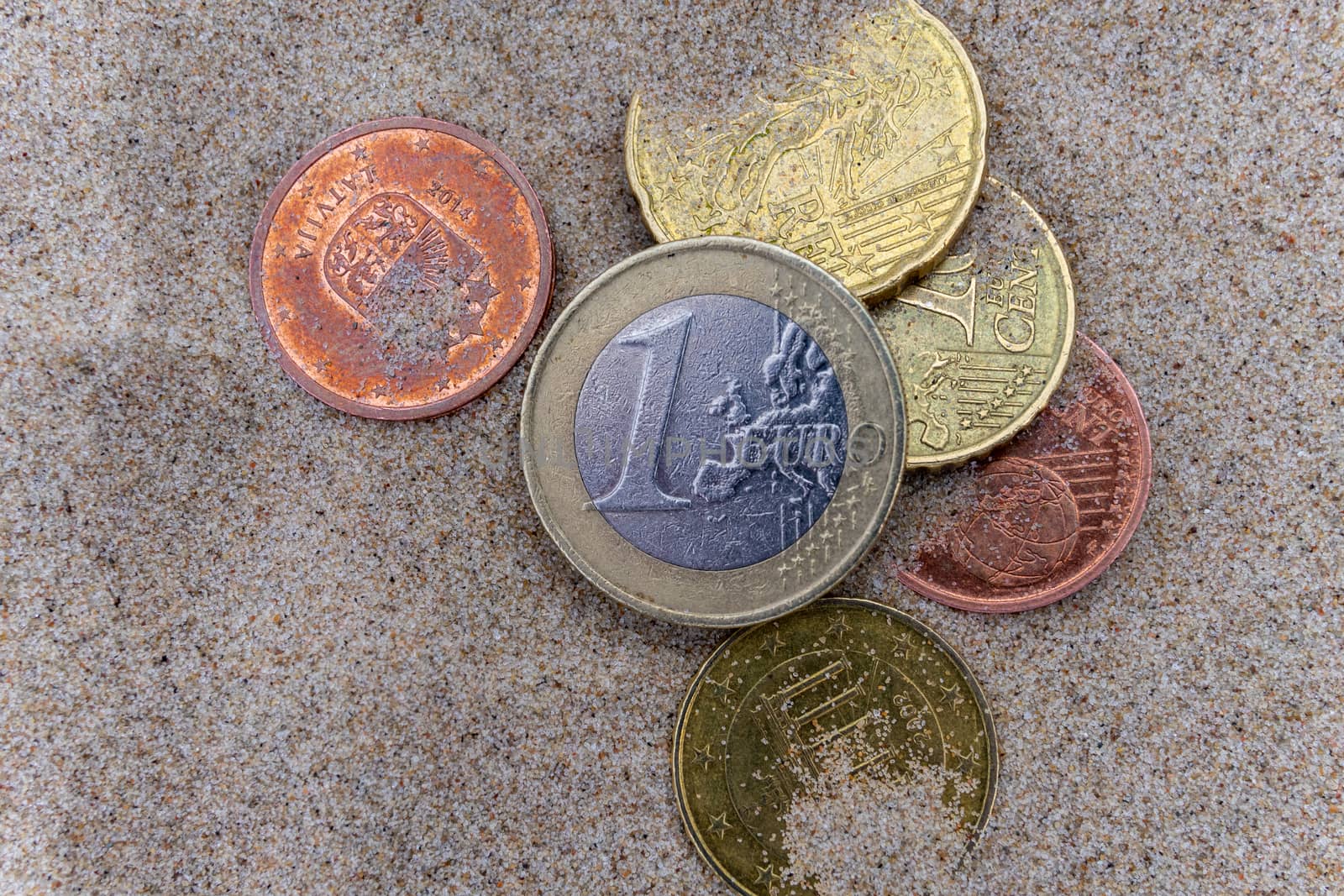1 euro coin on the wet fine sand of a sea beach.