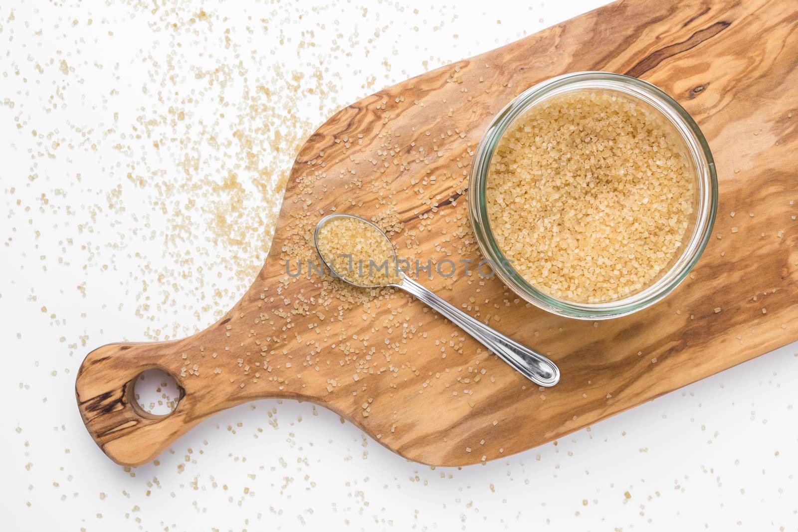 Organic brown sugar in glass jar on wooden chopping board. Top view.