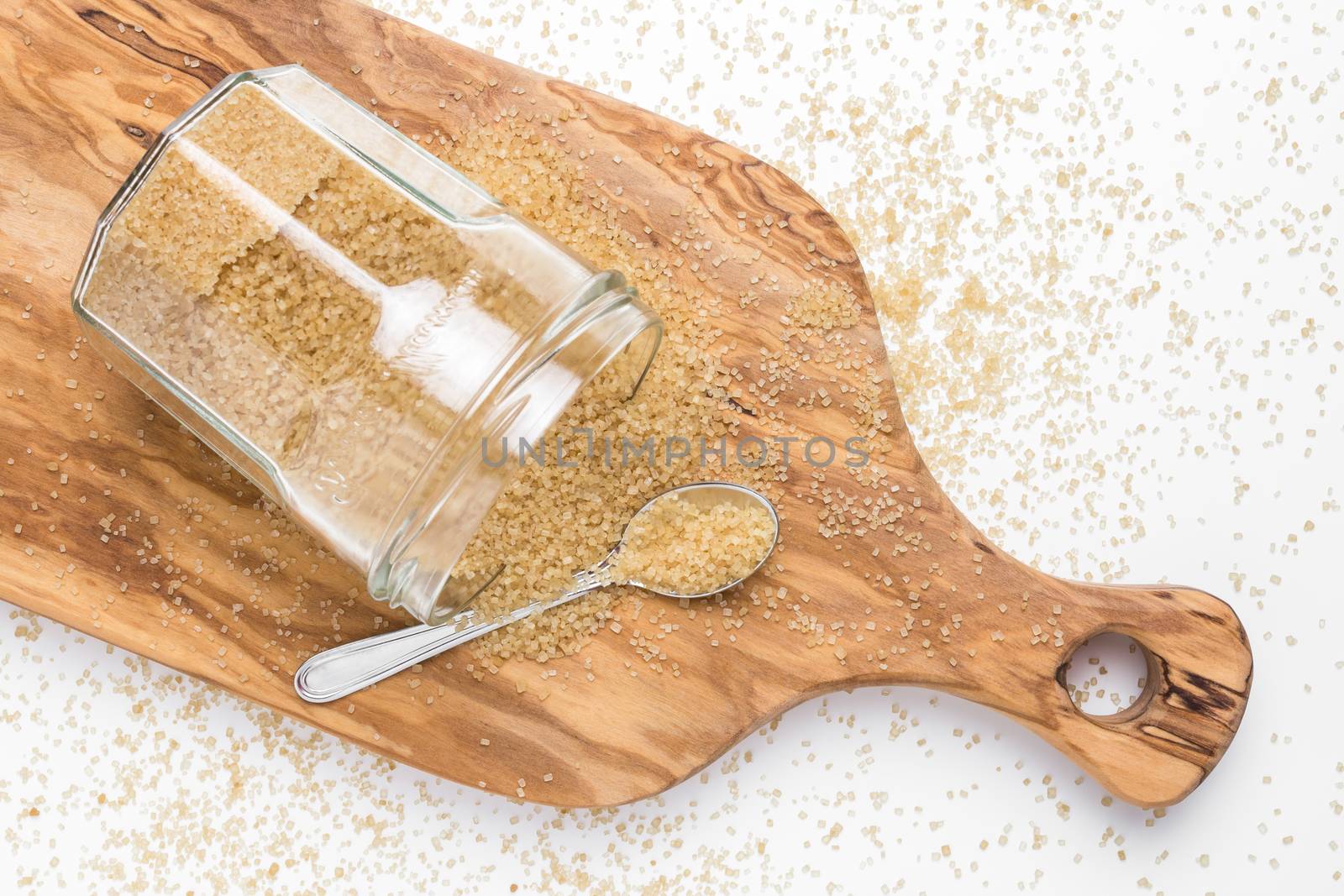Organic brown sugar in glass jar on wooden chopping board. Top view.