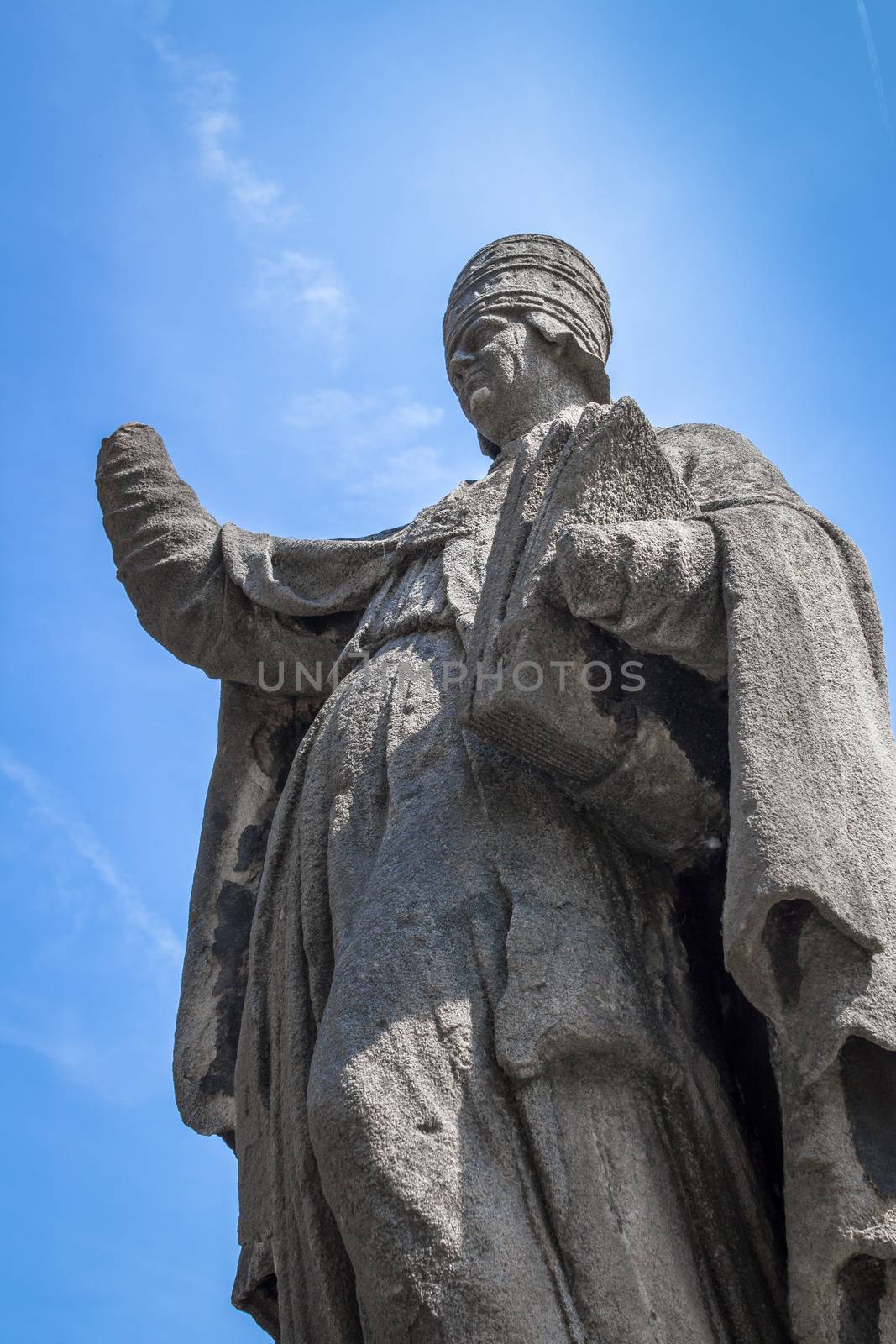 Statue of a pope with mutilated hands, against a blue sky and sunlight.