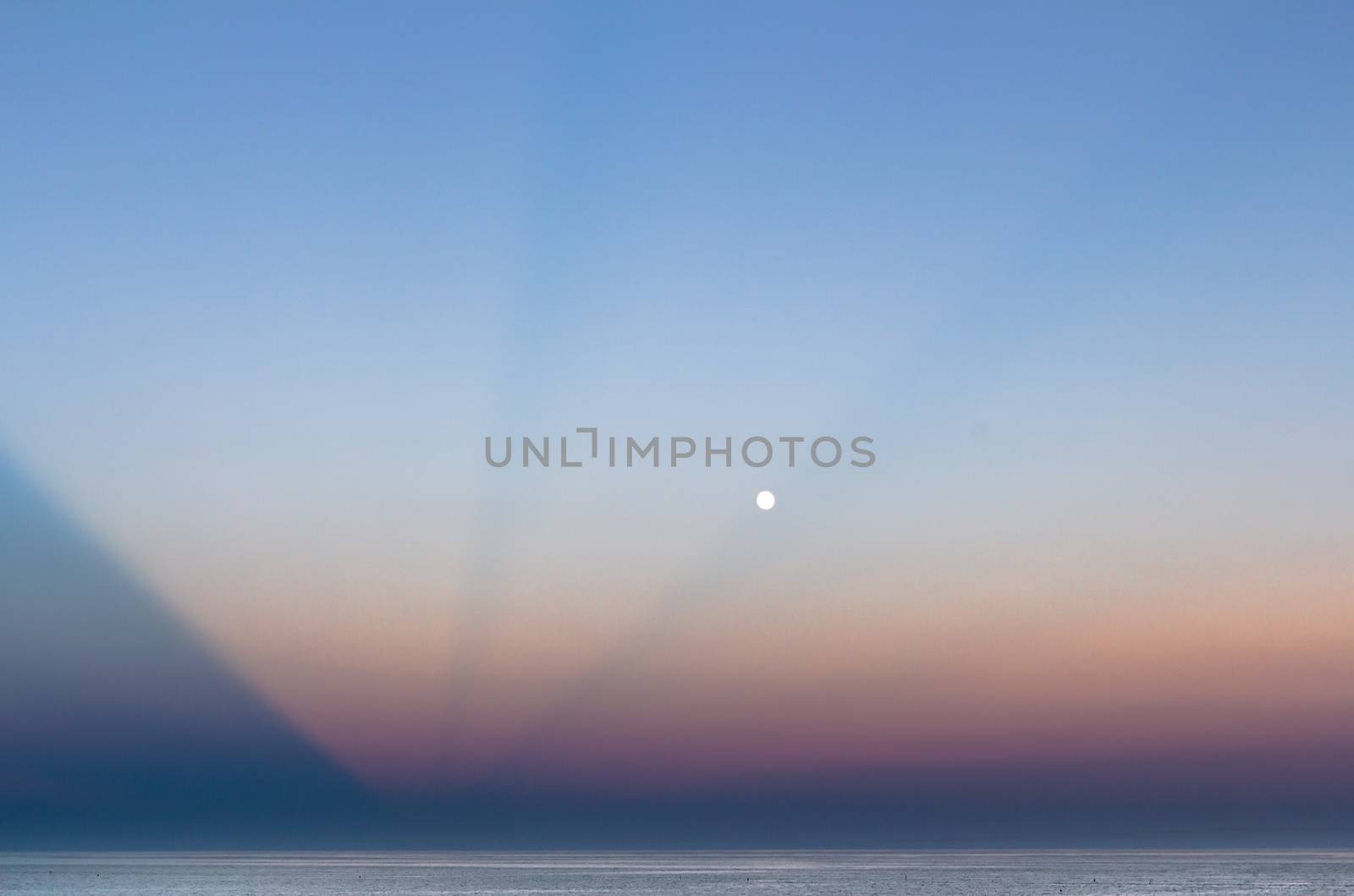 Abstract and dramatic sunset with light rays that create the shape of an inverted pyramid on the sea.