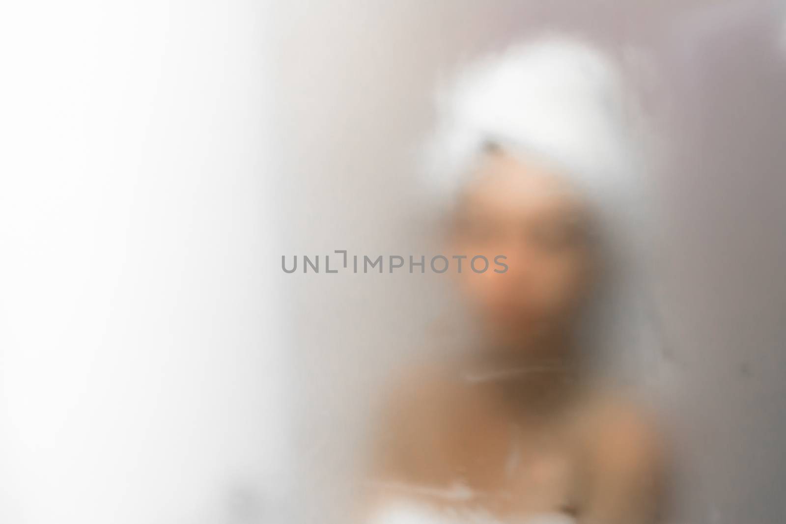 Young woman reflected in the mirror blurred by the steam. Defocused blurry background.