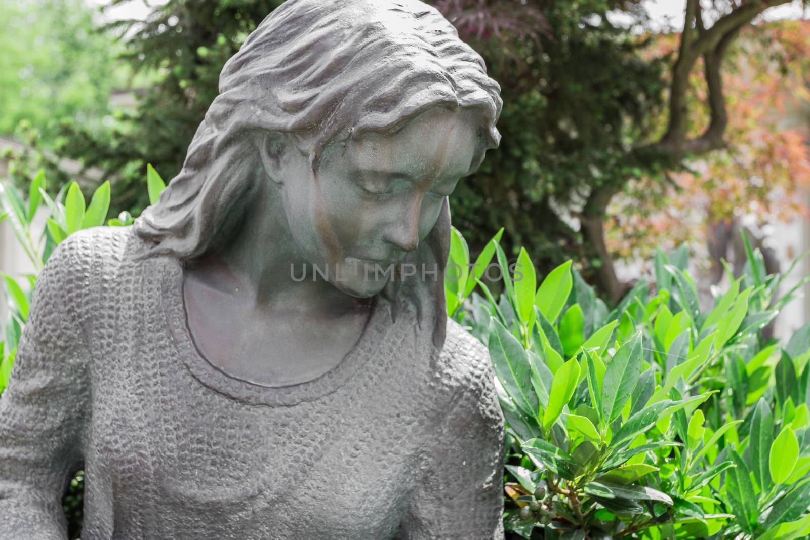 Statue of a long-haired girl. On background green plants.