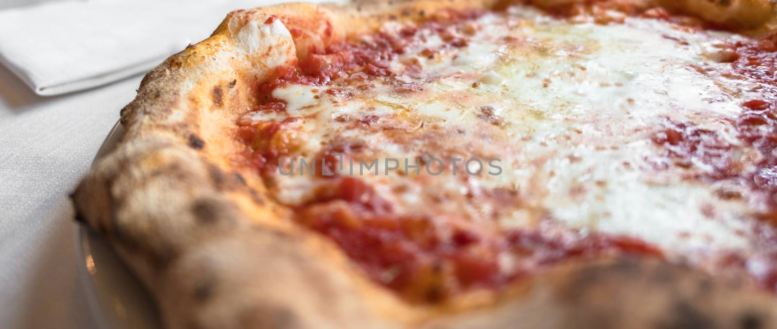 Pizza margherita, typical Italian plate. In the background an elegant white tablecloth.