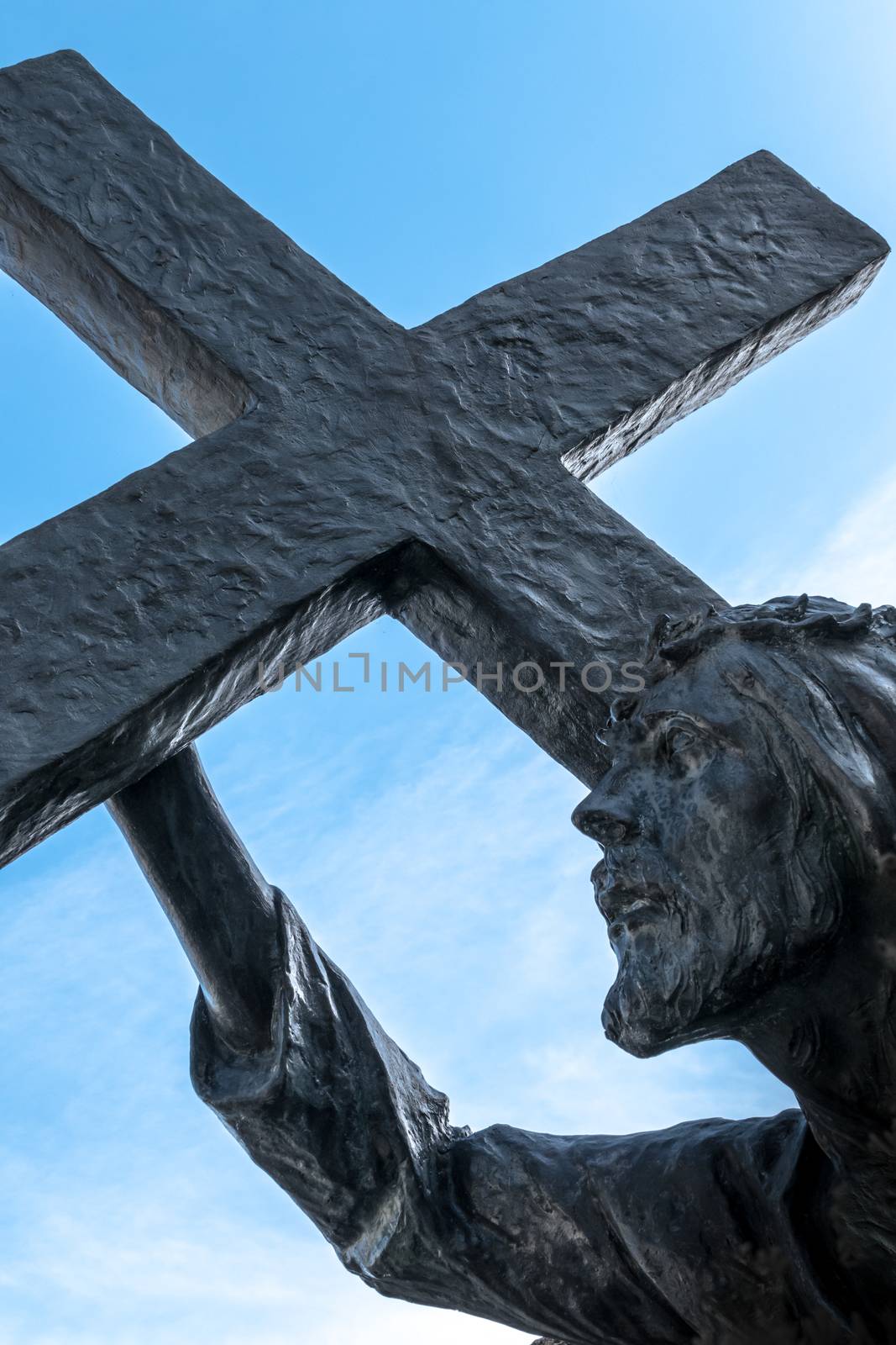 Bronze statue of Jesus carrying his cross, on the way to his crucifixion. Ideal for the easter concept, resurrection and other. Blue sky with white clouds on background.