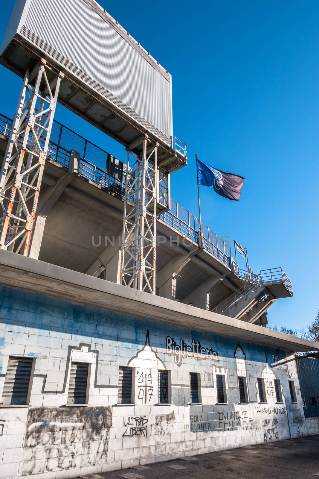 The exterior of the football stadium where Atalanta plays. Atalanta flag. On the old wall, graffiti with the text "biglietteria". On background a blue sky. Bergamo, italy - December 10, 2018