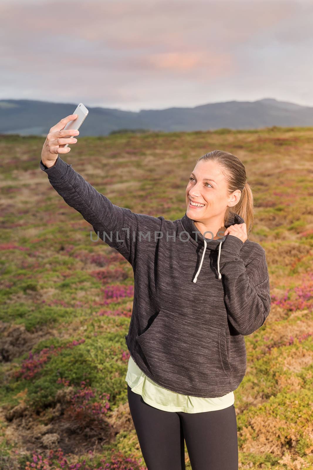 Girl taking a self-portrait with a mobile phone in the park at sunset by JRPazos