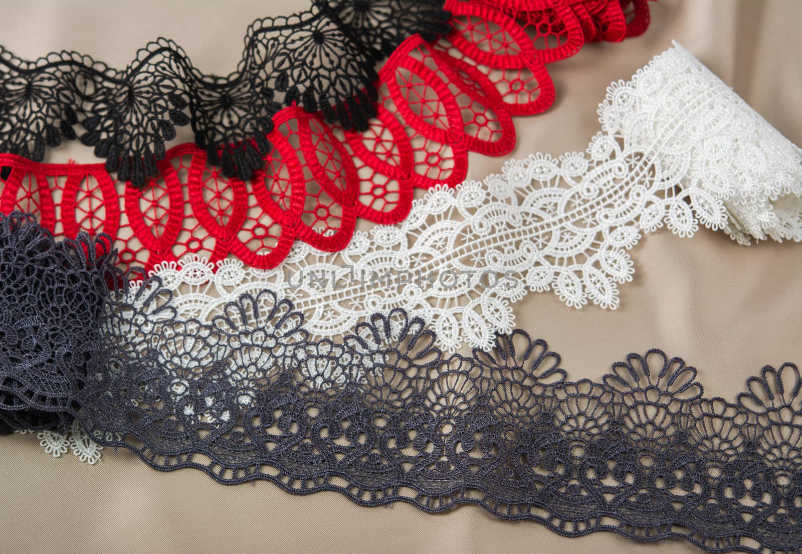 pile of red, white. black and gray gentle luxury quality guipure, lace fabric on beige background. use for sew clothes linen decoration. texture for websites