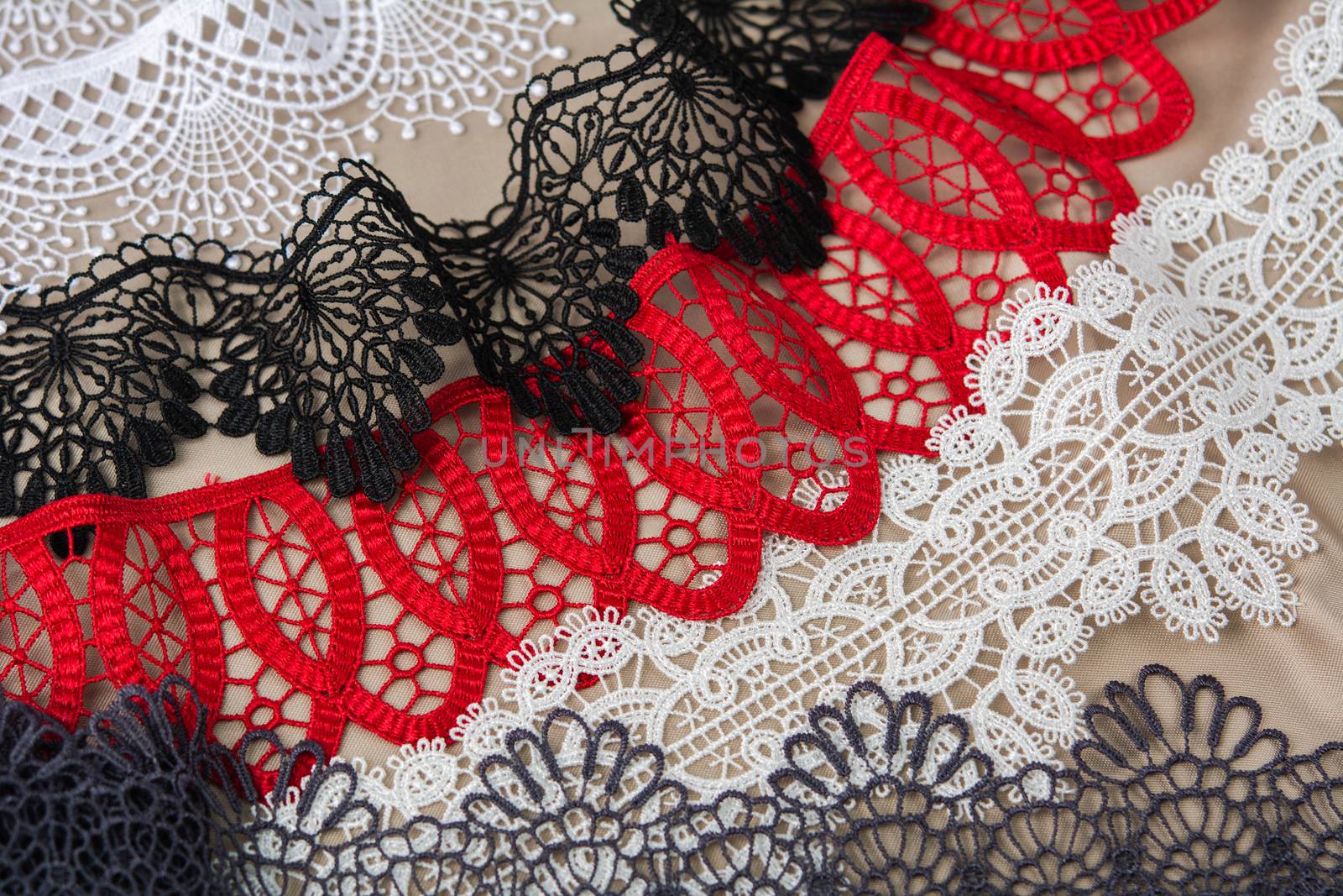 pile of red, white. black and gray gentle luxury quality guipure, lace fabric on beige background. use for sew clothes linen decoration. texture for websites