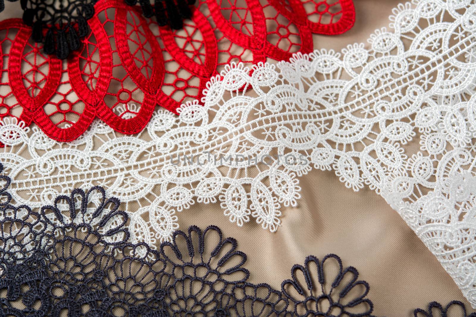 pile of red, white. black and gray gentle luxury quality guipure, lace fabric on beige background. use for sew clothes linen decoration. texture for websites