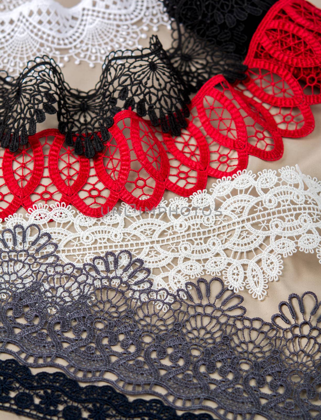pile of red, white. black and gray gentle luxury quality guipure, lace fabric on beige background. use for sew clothes linen decoration. texture for websites
