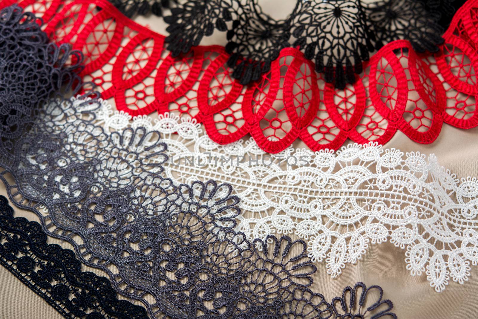 pile of red, white. black and gray gentle luxury quality guipure, lace fabric on beige background. use for sew clothes linen decoration. texture for websites