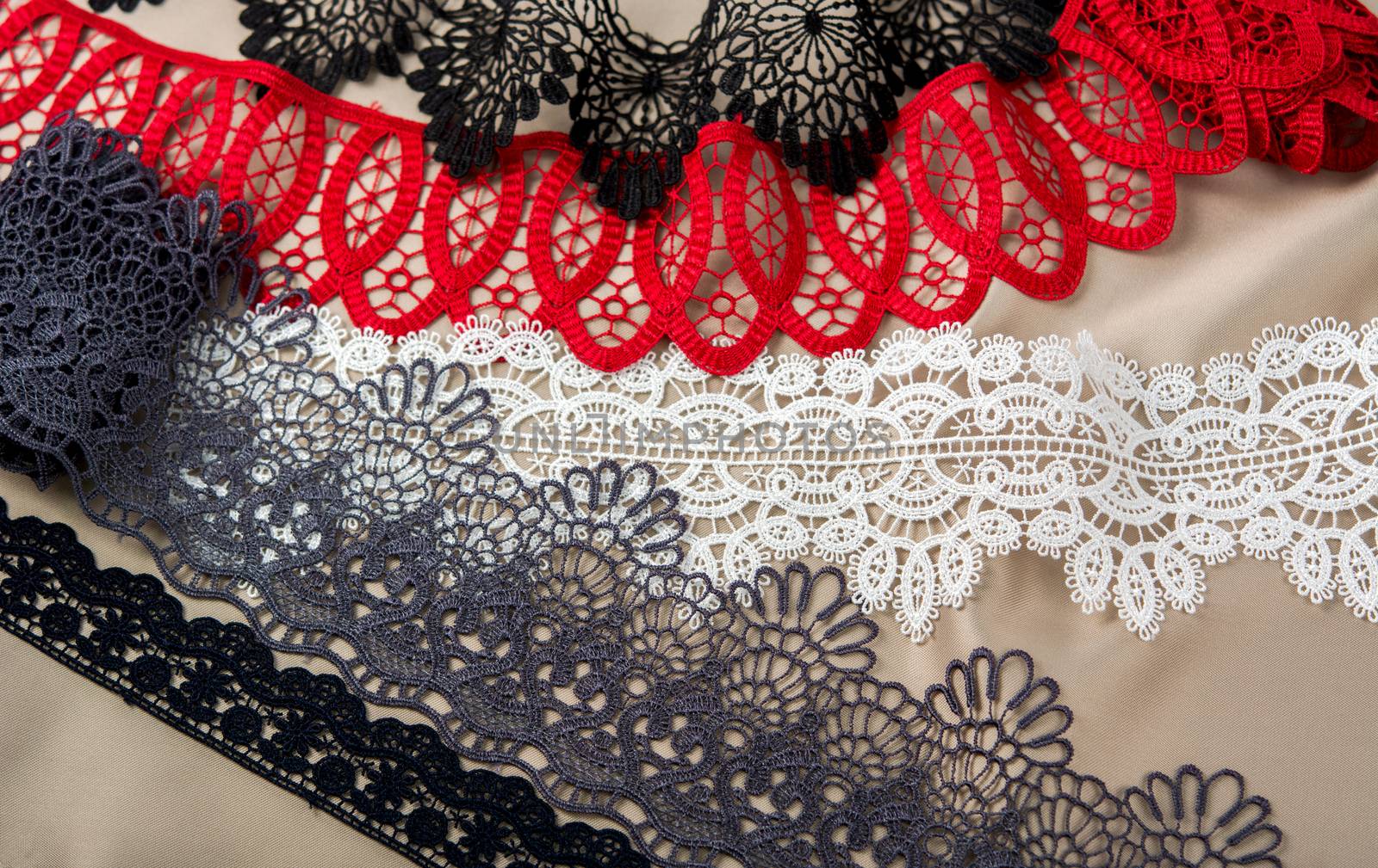 pile of red, white. black and gray gentle luxury quality guipure, lace fabric on beige background. use for sew clothes linen decoration. texture for websites