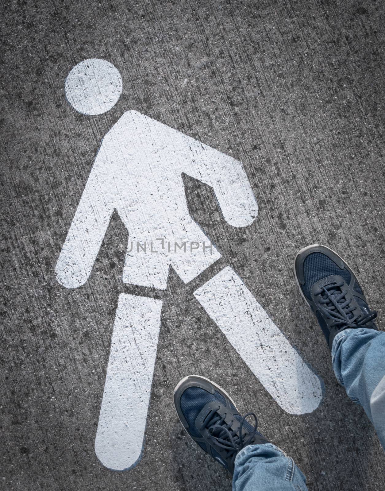 Man in sports shoes standing on the asphalt road, near at the pedestrian horizontal road sign.