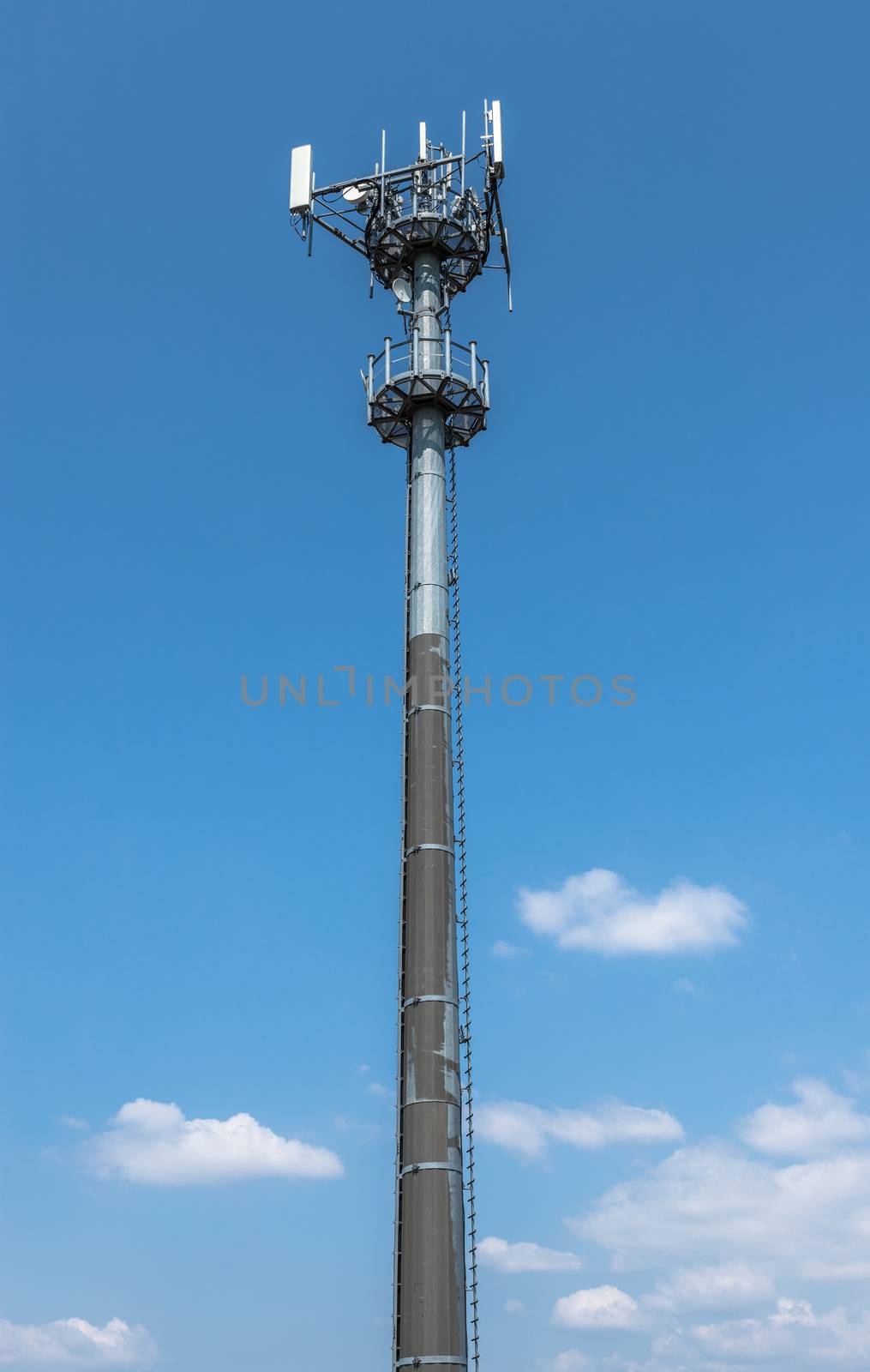 A communications tower for mobile phone signals, against a blue sky background with white clouds.