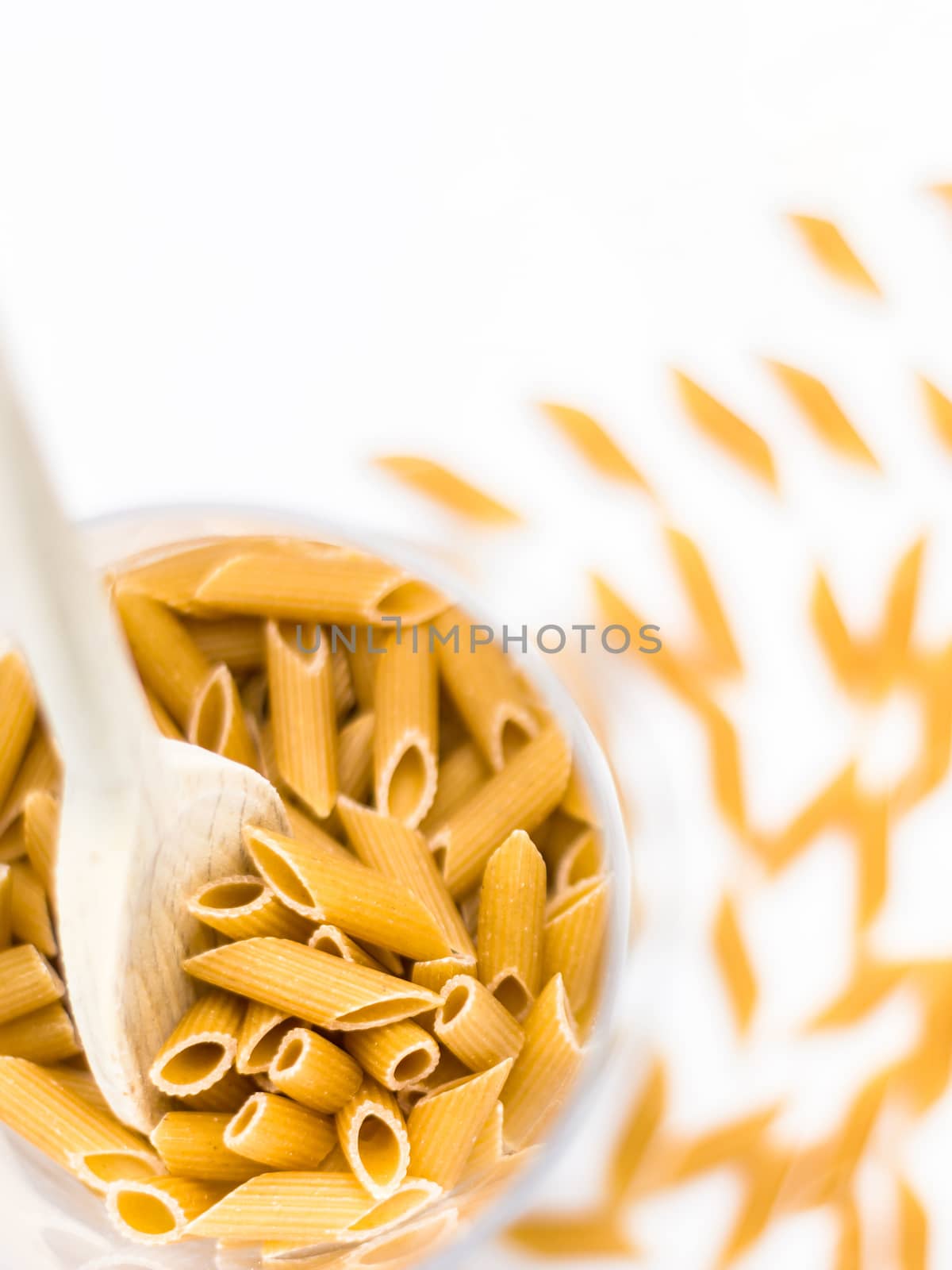 Close up of whole pasta in a glass bowl and wooden spoon on white background. Copy space.