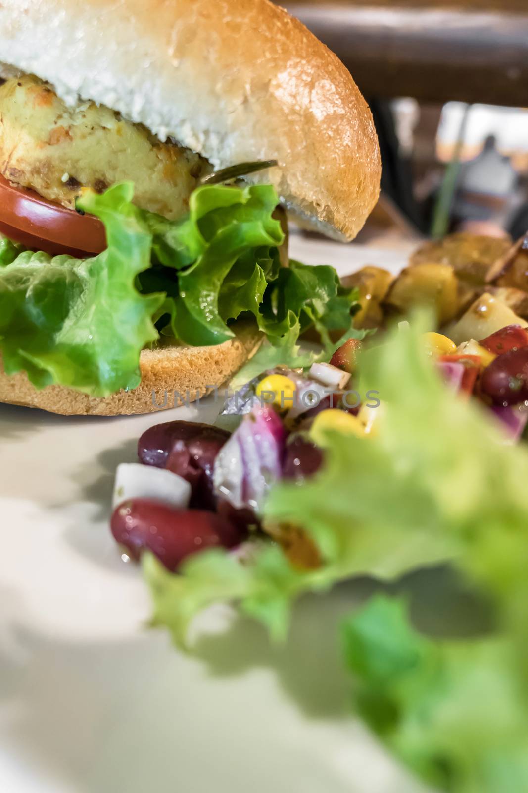 Healthy vegan burger with tomato, baked potatoes, beans, onions, salad. Close-up.