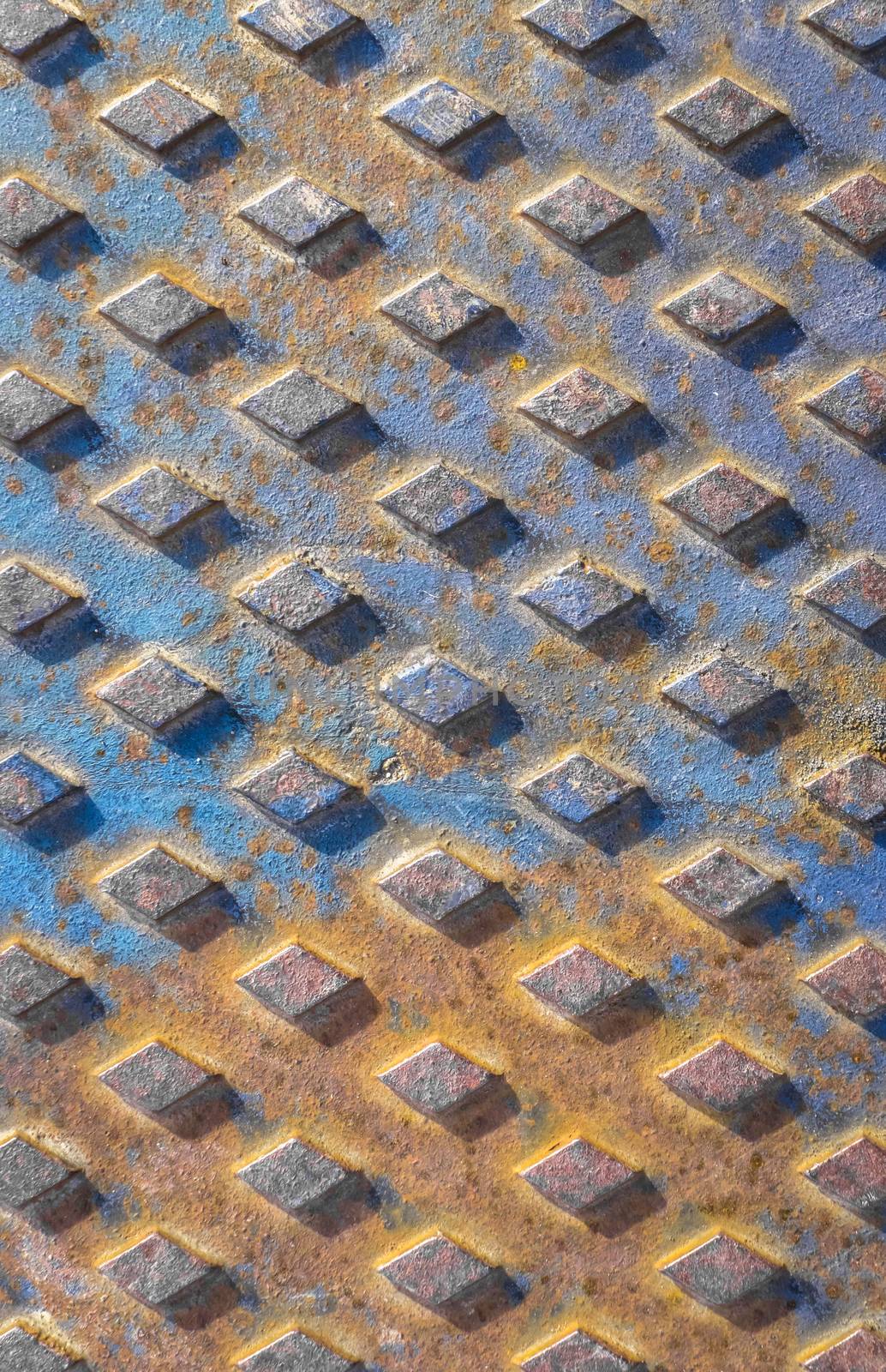 Old rusty drain cover background with diamond pattern. Orange and blue rusted manhole texture with square pattern, background macro.