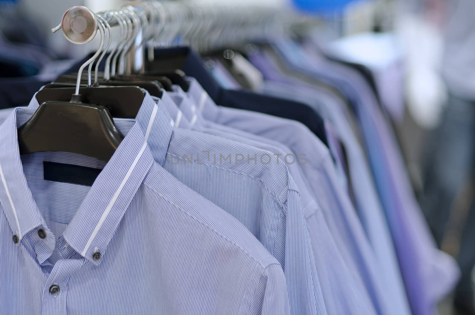 Blue striped collared shirt on coathanger on long clothes rack. Shallow focus on shirt at front. 