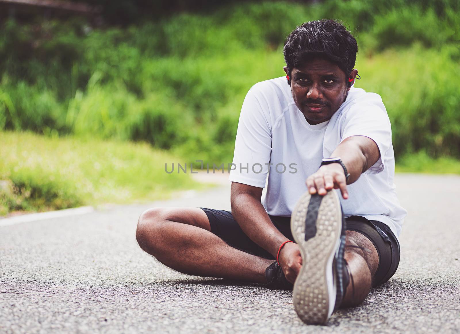 Close up Asian young athlete sport runner black man wear watch he sitting pull toe feet stretching legs and knee before running at outdoor street health park, healthy exercise before workout concept