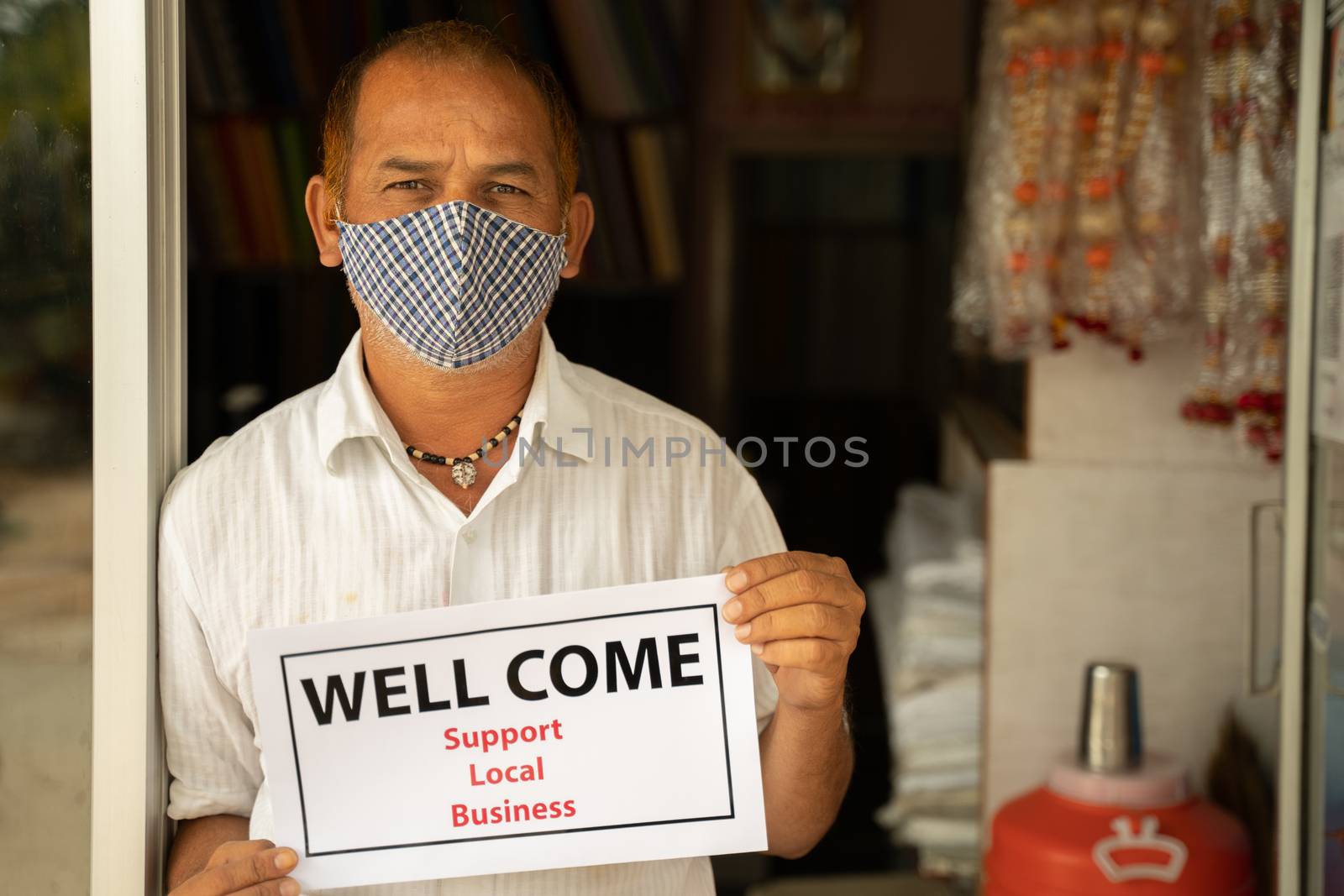Small business owner in medical mask holding Wellcome notice infront of door after store reopening during coronavirus or covid-19 - concept of support local business and restart work after pandemic. by lakshmiprasad.maski@gmai.com