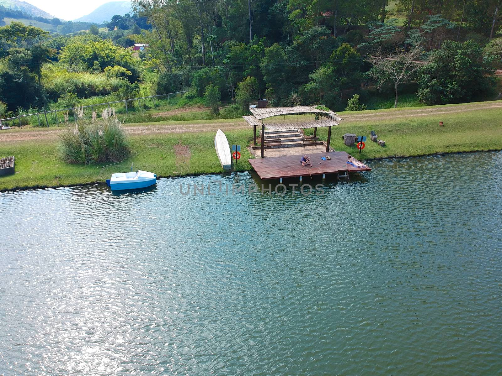 Aerial view of beautiful little wood cabana next the water of a lake, fisher on the dock of the little hut trying to catch fish. relax moment next the water in the sun.