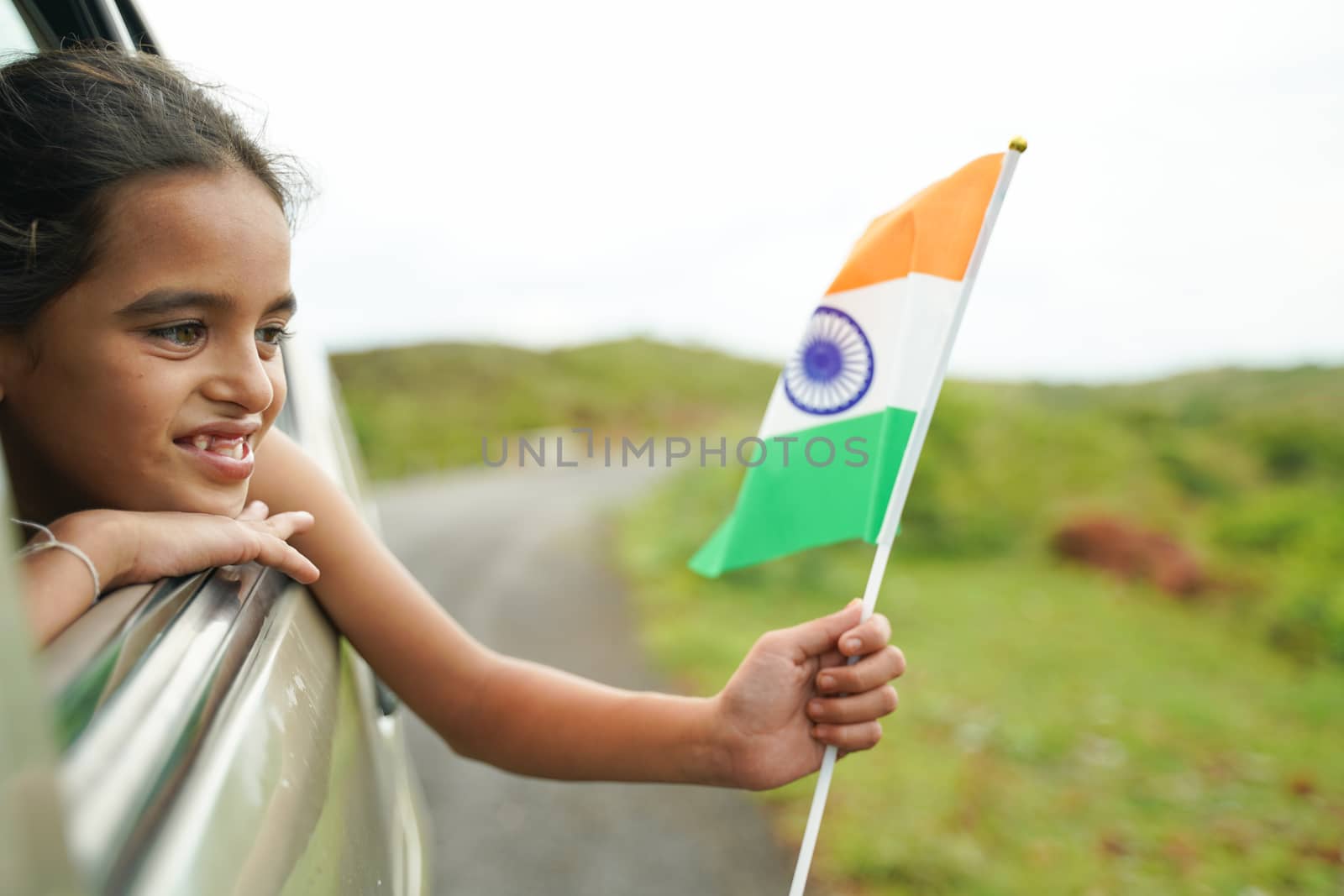 Happy Cheerful Young girl kid holding Indian flag out of in moving car window - Concept of patriotism and Independence or republic day celebration by lakshmiprasad.maski@gmai.com