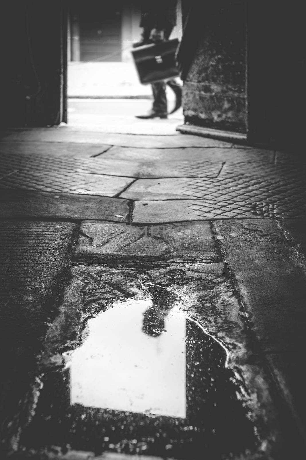 Business man on the street. His head is deliberately cut from the frame and visible in the puddle. Loneliness, stress or unemployment concept. Black and white and retro style photo.