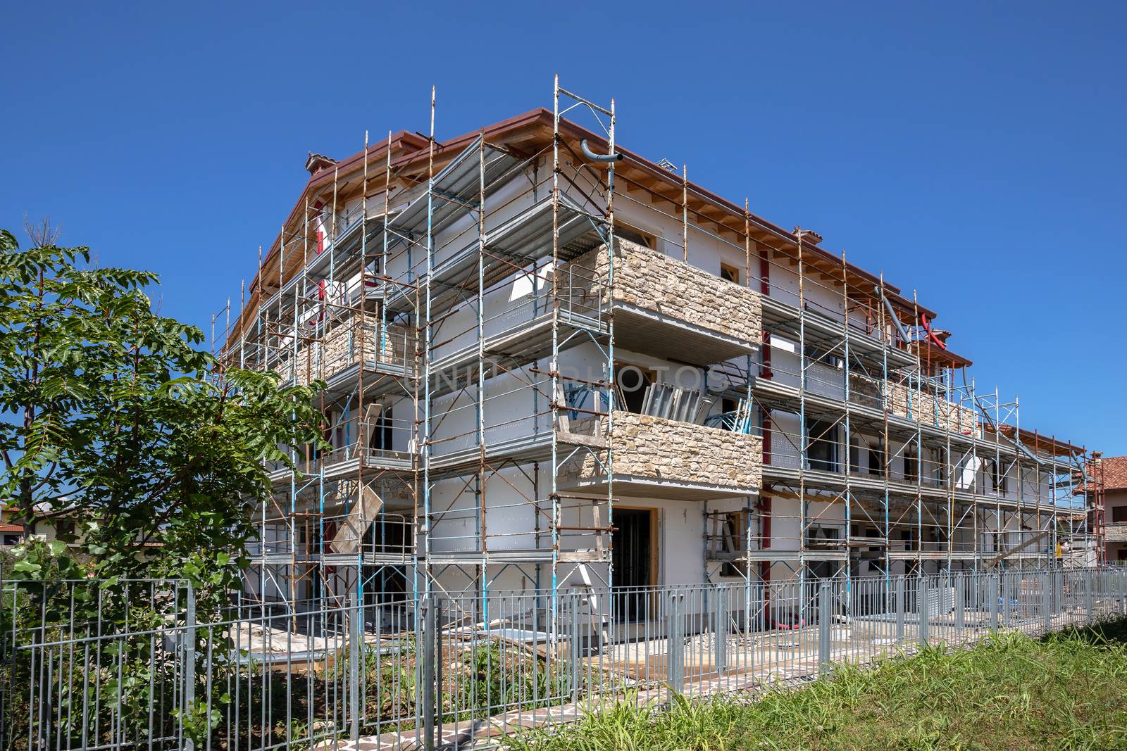 Scaffolding near a house under construction for external plaster works. Modern apartment building in city with stone balconies.