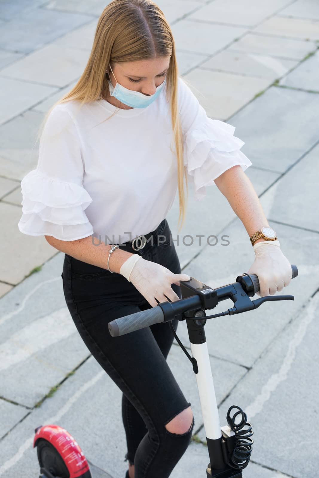 Trendy fashinable girl wearing corona virus protective face mask and rubber gloves while using rental electric scooters in city environment. Eco-friendly city transport in Ljubljana, Slovenia by kasto