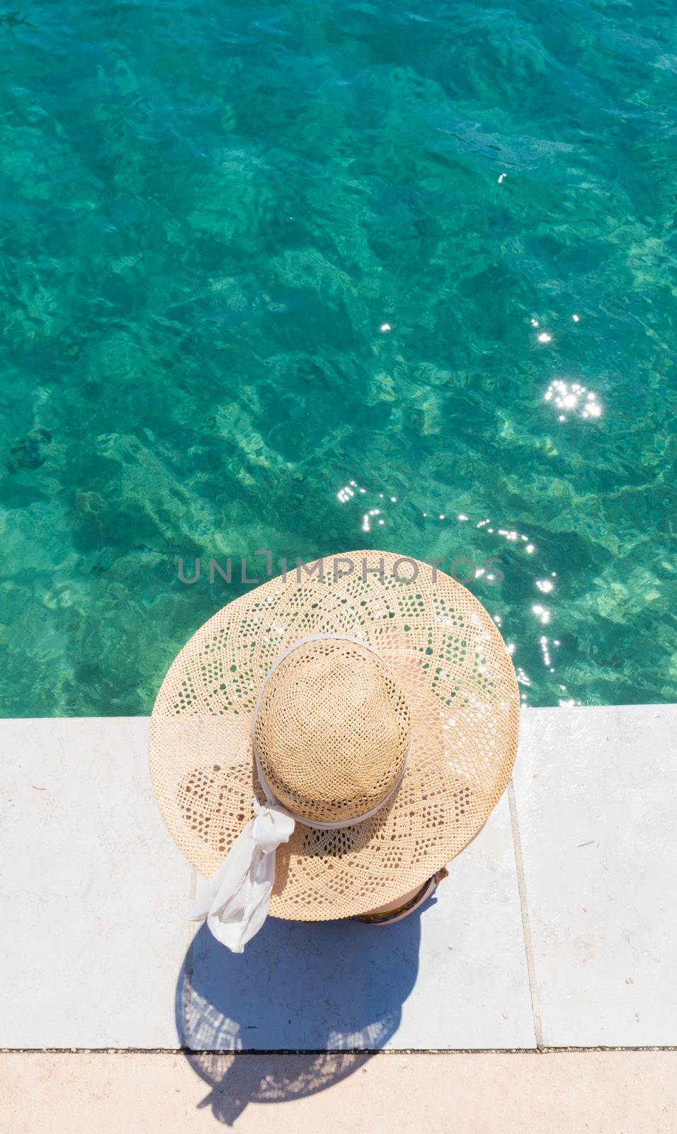 Woman wearing big summer sun hat relaxing on pier by clear turquoise sea. by kasto