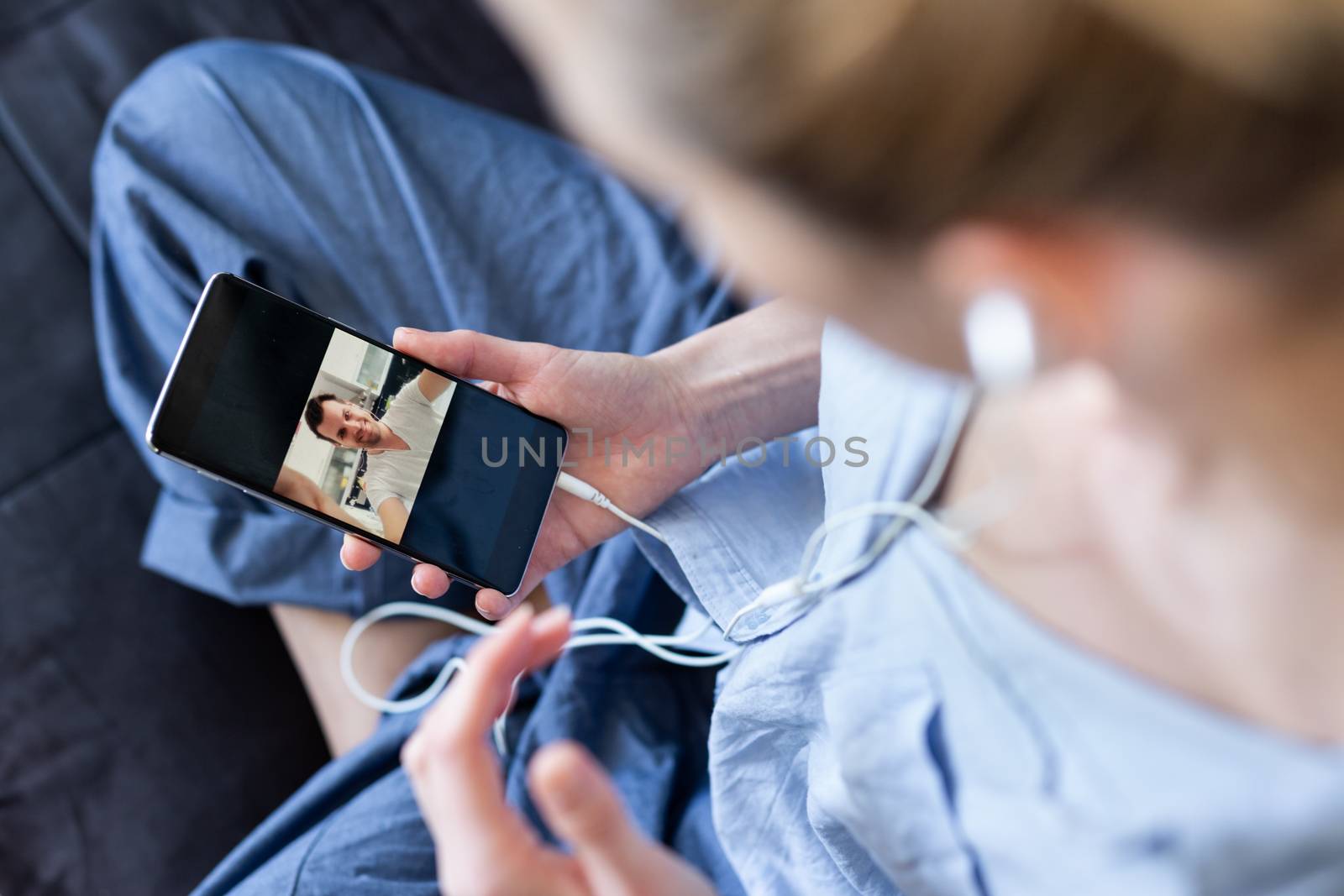 Woman at home relaxing on sofa couch using social media on phone for video chatting with her loved ones during corona virus pandemic. Stay at home, social distancing lifestyle. by kasto