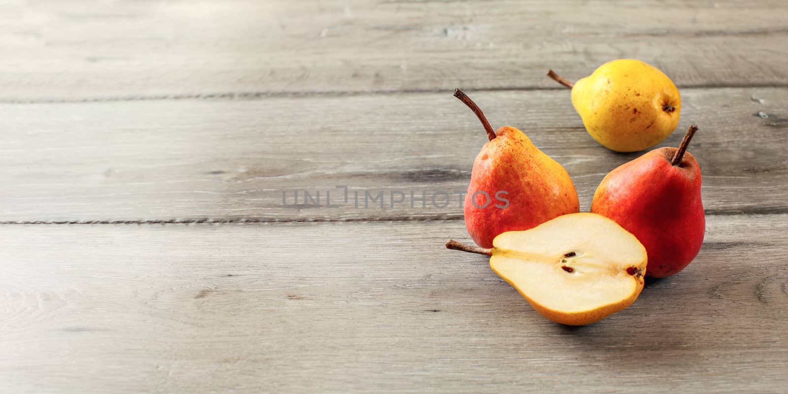 Top view of ripe pears, one of them cut in half, on gray wooden table.