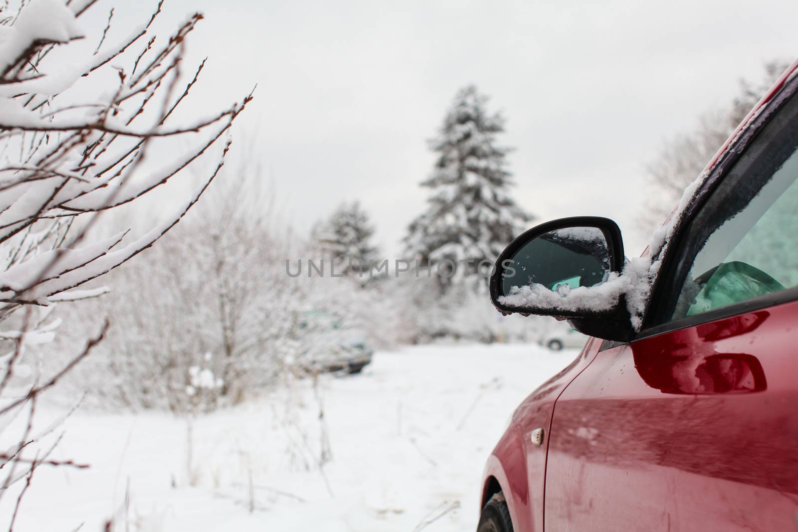 Detail on mirror of red car parked on a winter road with snow co by Ivanko