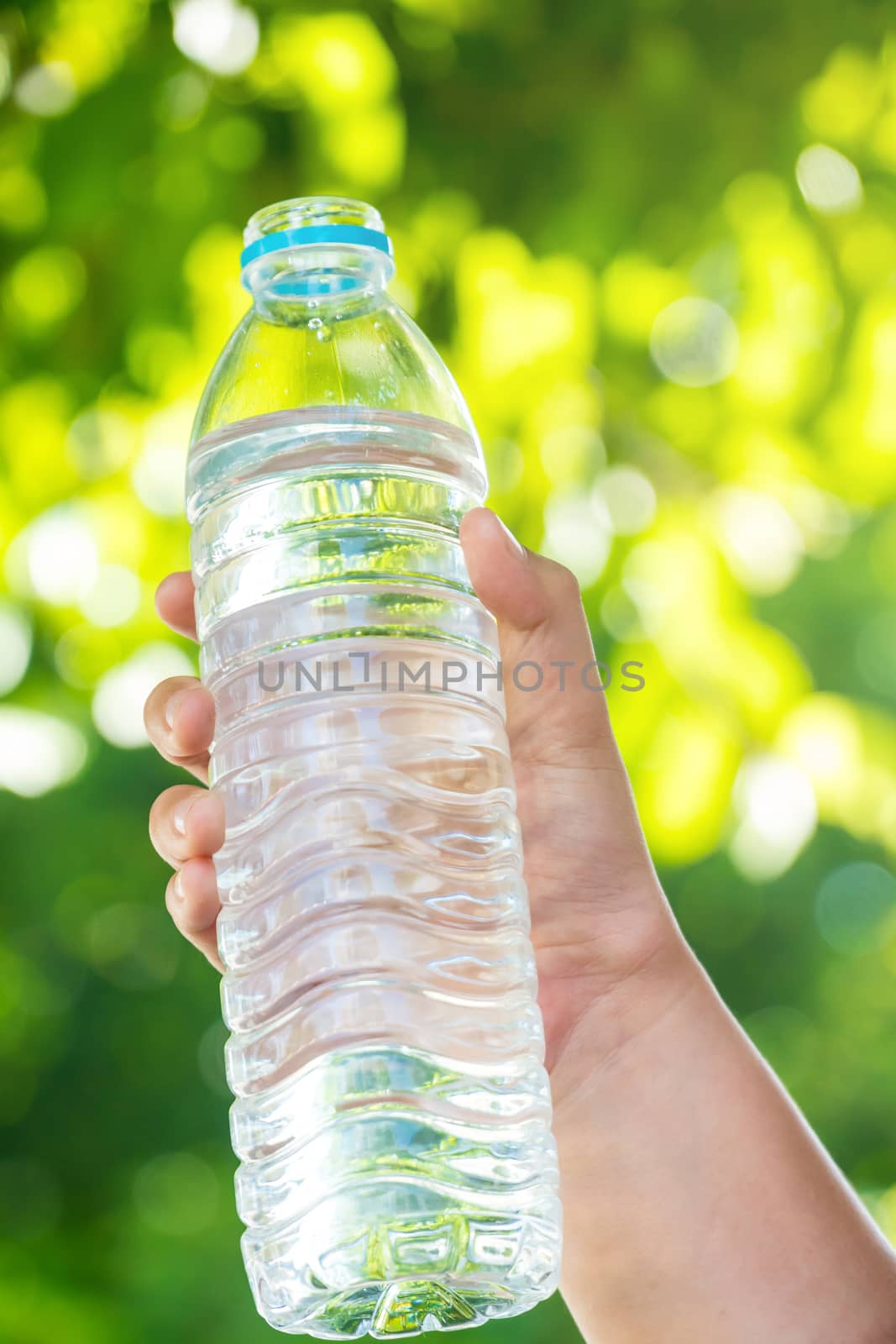 The boy's hand is holding a bottle of water on a natural background