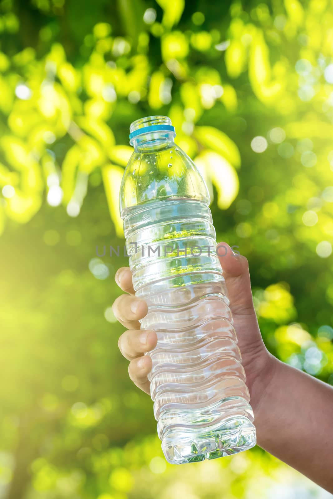 The boy's hand is holding a bottle of water on a natural background