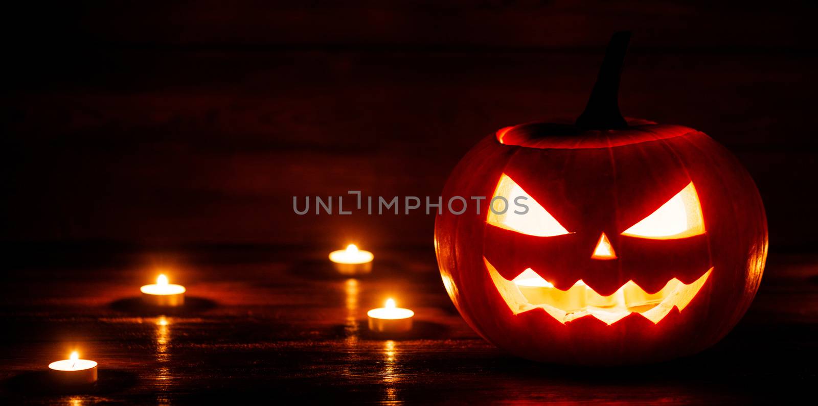 Halloween pumpkin head jack o lantern and candles on wooden background