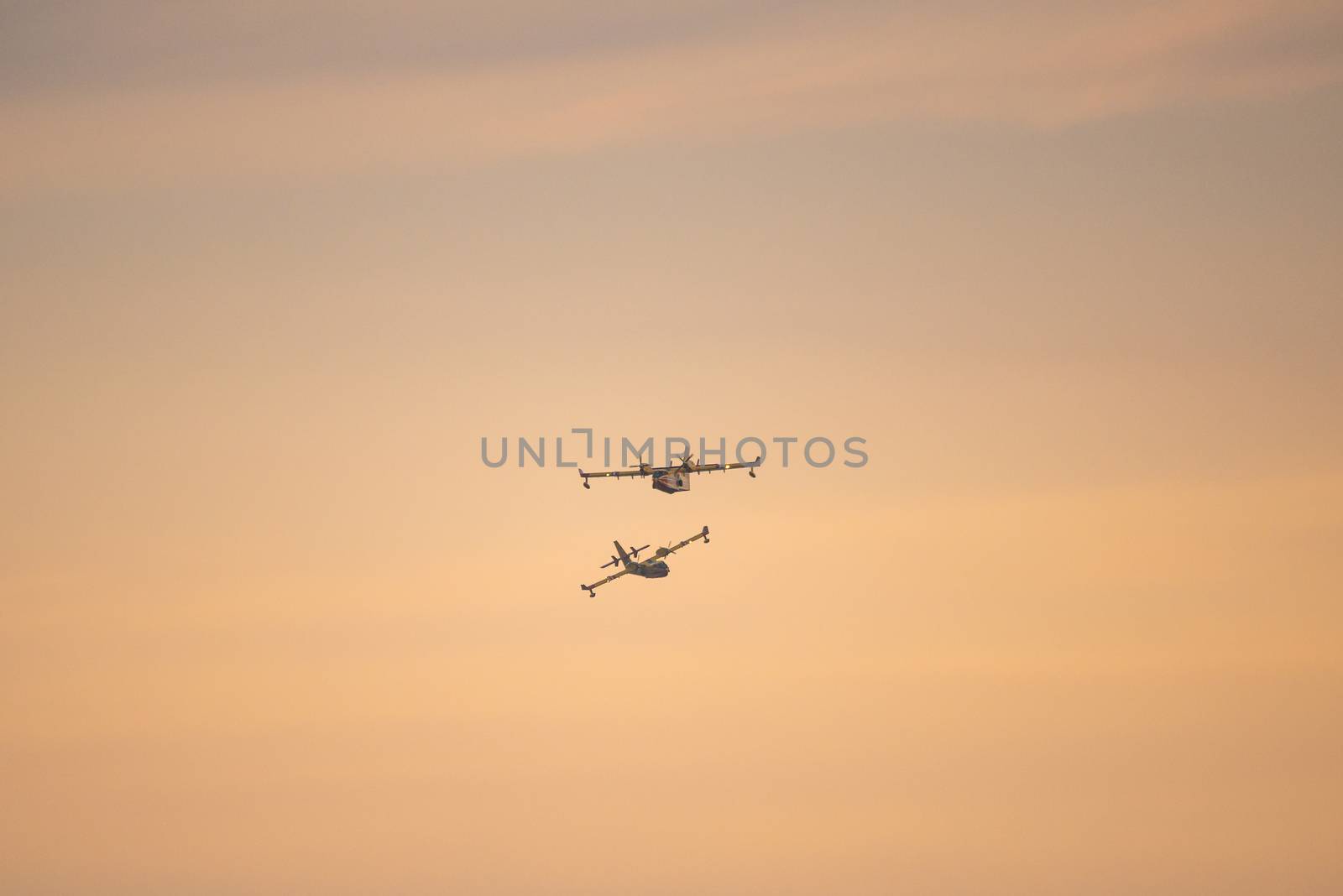 Two amphibious water bomber airplanes in flight at sunset, in France.