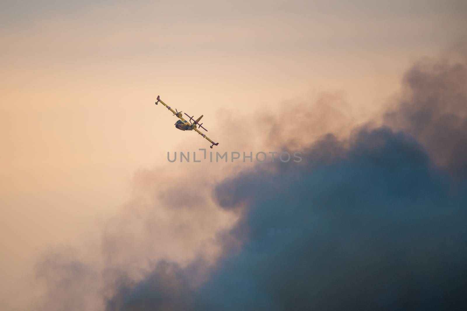 Amphibious water bomber airplane in flight at sunset, smoke from a forest fire, in France.