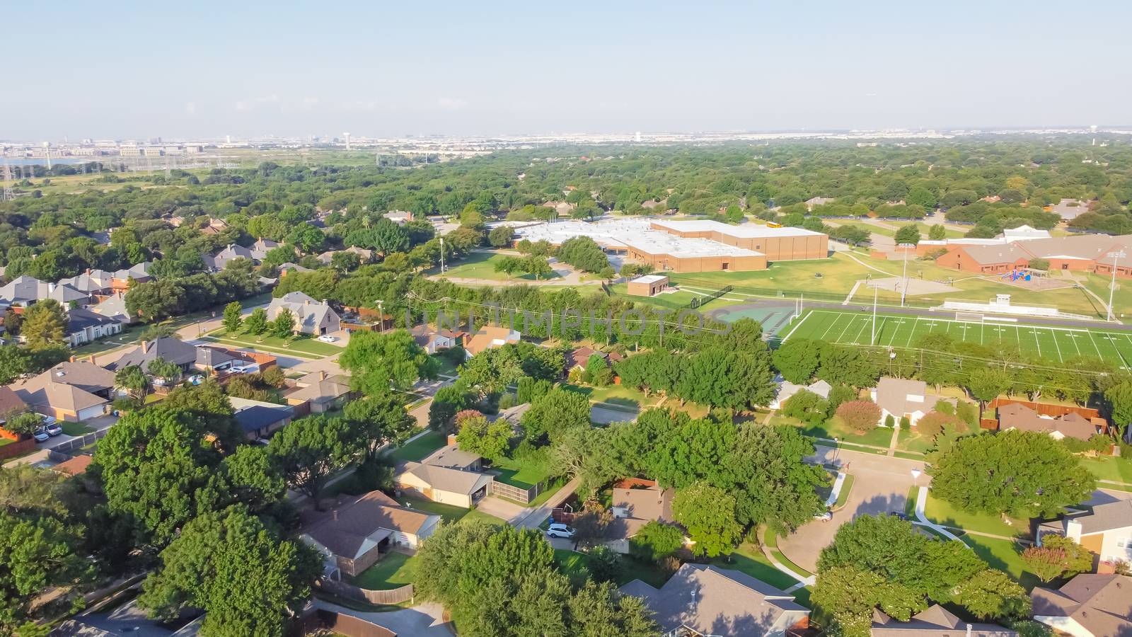 Residential neighborhood in school district with football field in background near Dallas, Texas, America. Suburban houses with large fenced backyard and large tree in early summer morning light