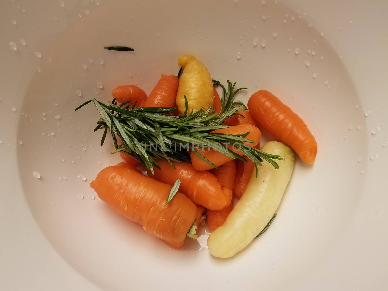 orange carrots and rosemary in white container or bowl